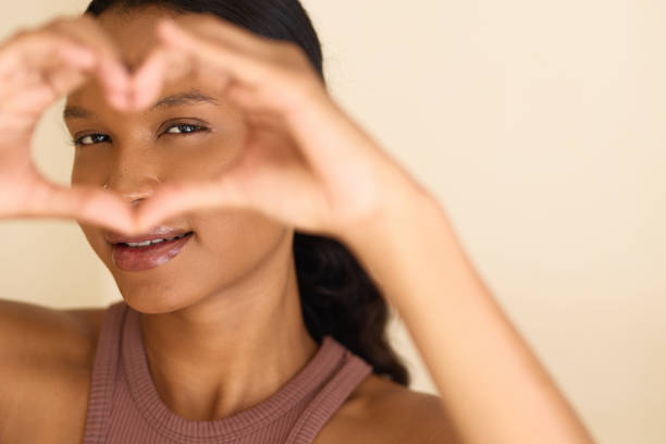 istock Smiling Woman Framing Face with Heart Gesture in Warm Light 2187542347