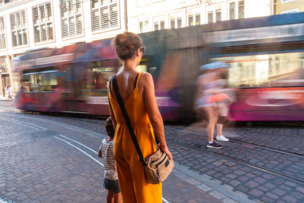 A woman in a yellow dress is walking down a street with a child in a striped outfit. She is carrying a handbag and she is in a hurry. freiburg im breisgau; freiburg