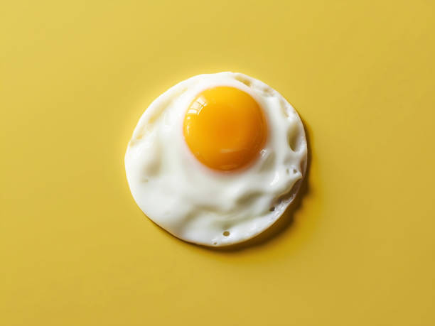 istock Flat lay image of a single sunny-side-up egg, perfectly centered and isolated on a bright, vibrant yellow background 2187547904