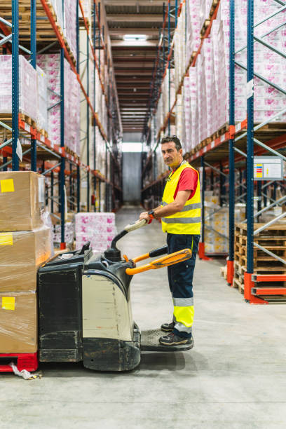istock Warehouse worker moving boxes with pallet truck in logistics center 2187549067