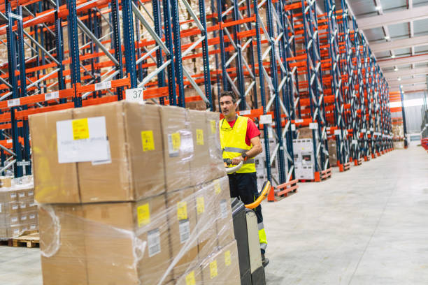 istock Warehouse worker moving boxes with a pallet jack in a logistics center 2187549071