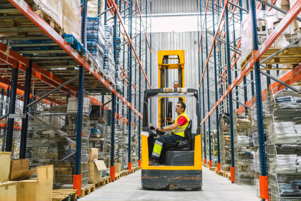 istock Warehouse worker driving forklift between shelves full of goods 2187549155