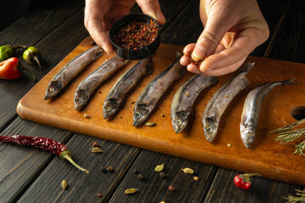istock Hands skillfully sprinkle spices over fresh fish lined on a wooden board, surrounded by vibrant herbs and chilies. A fusion of flavors awaits in this culinary creation. 2187552637