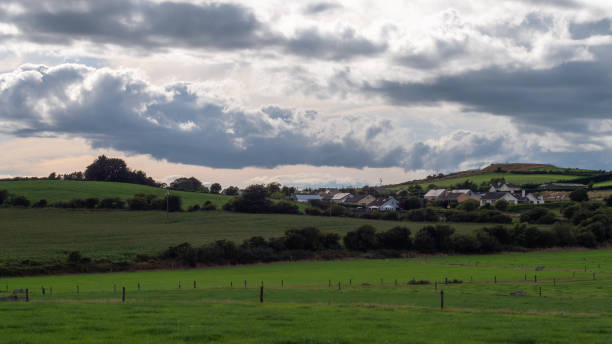 istock A small Irish village among green fields and trees under a cloudy evening sky, County Cork. Rustic Irish landscape in summer, European village. Green grass field under sky 2187554500