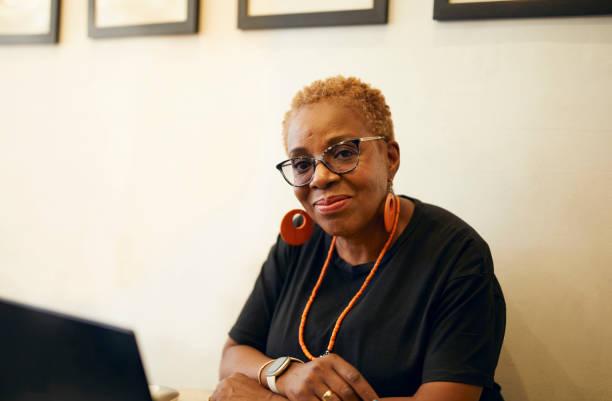 An African middle aged woman sat in a cafeteria checking her work email while waiting for coffee