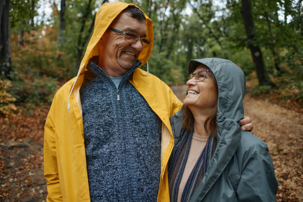 istock Happy mature couple in raincoats during rain in forest 2187557459