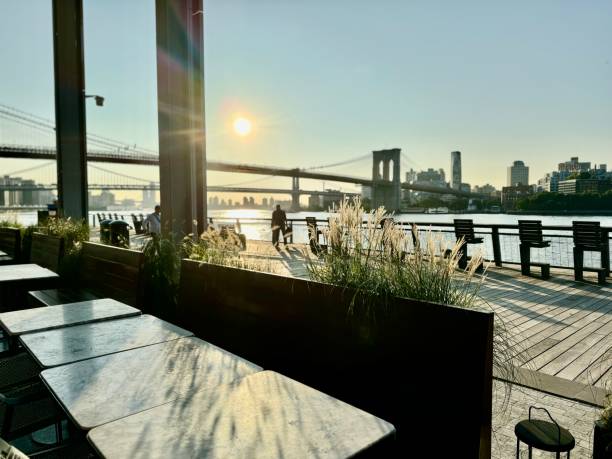 istock A table at a riverside restaurant with the sun setting over the Brooklyn Bridge in the background. 2187564006