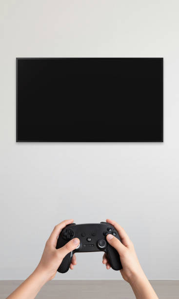 istock Blank TV mounted on a wall with a gamepad in hands, vertical composition, ideal for promoting video games and immersive home entertainment setup 2187566529