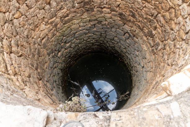 istock Round stone well with water reflecting sky and fallen branches 2187567312