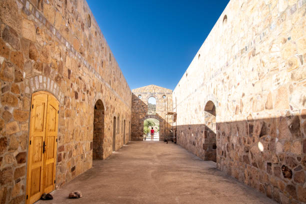 istock Long stone corridor with arches, wooden doors, and scaffolding under a clear blue sky 2187567316