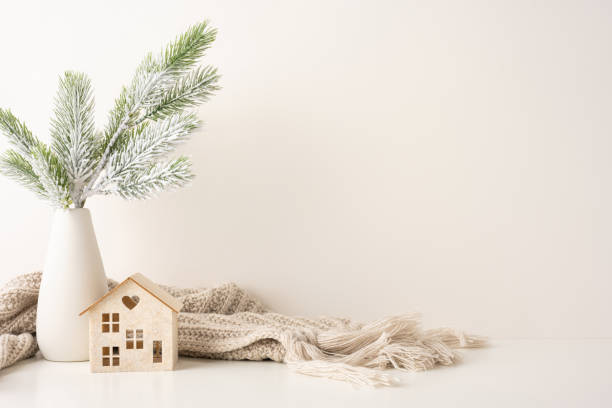 istock A side view minimalist winter decor setup featuring a frosted pine branch in a vase beside a cozy scarf and wooden house model, evoking a Scandinavian Christmas theme 2187575565