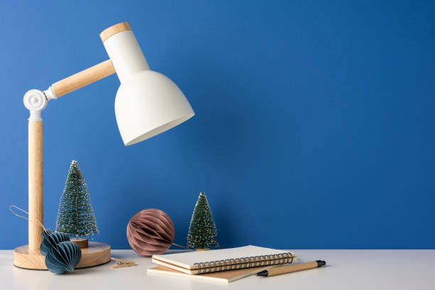 istock A side view stylish minimalist workspace featuring a wooden lamp, notebook, and festive Christmas decorations against a blue wall. Ideal for winter-themed or Scandinavian-style design inspirations 2187575589