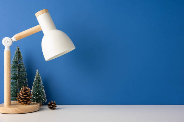 istock A side view minimal scandinavian workspace featuring a desk lamp, small pine trees, and pine cones on a blue background. The setting exudes a cozy winter atmosphere 2187575614