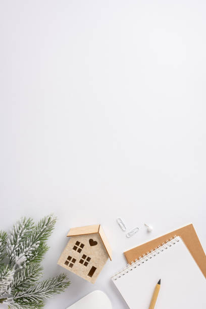 A vertical warm and inviting winter-themed workspace featuring a notebook, pencil, paper clips, and a decorative pine branch. Ideal for creative projects or holiday planning