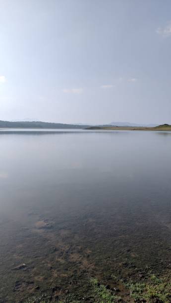 istock Serene lake with still waters, grassy shorelines, and hazy distant hills under a clear blue sky 2187580938