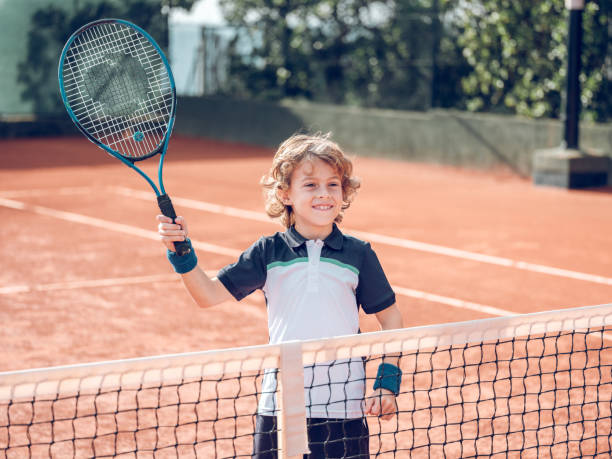 istock Positive kid raising racket while playing tennis on court 2187583942