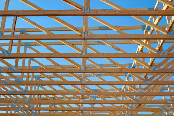 Workers build the frame of a new house project. Bare plywood and beams as it is framed up from the foundation. High lumber costs have affected the building process.  A crane lowers assembled rafters and trusses.  Shot in Washington state, USA.
