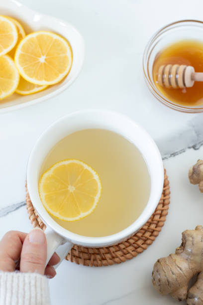 istock Hand holding ginger root and lemon tea cup with honey on white marble table, top view 2187588384