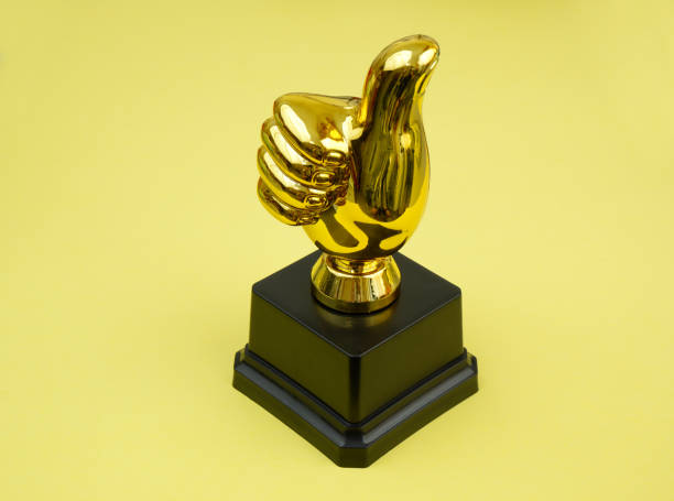 istock Thumbs up trophy cup on yellow background. 2187590243