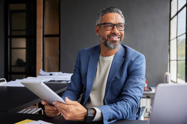 uśmiechnięty biznesmen korzystający z tabletu, wyglądający przez okno - lider zdjęcia i obrazy z banku zdjęć