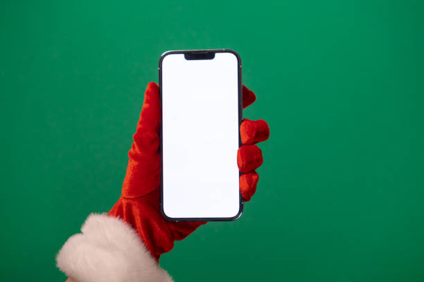 istock santa's hand in a red glove holding a smartphone with a blank white screen on a green background, perfect for christmas promotions or holiday app designs 2187601436