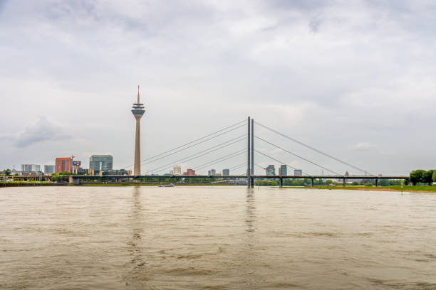 Dusseldorf, Germany - May 6, 2024: Scenic view of Düsseldorf's iconic Rheinturm tower and bridge spanning the Rhine River on a cloudy day, featuring modern architecture and waterfront charm. Perfect for travel, urban, and architectural themes