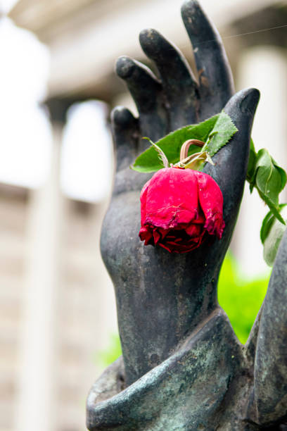 Hand of a copper sculpture of Christ, facing forward, holding a red rose. Symbol of peace and hope. Necrotourism. São João Batista Cemetery, Rio de Janeiro