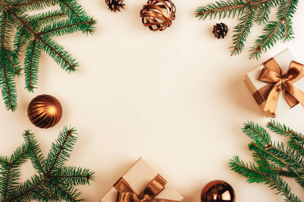istock Christmas-themed composition with green pine branches, bronze gift boxes with ribbons, and ornaments arranged on a beige background. Top view, flat lay 2187611494