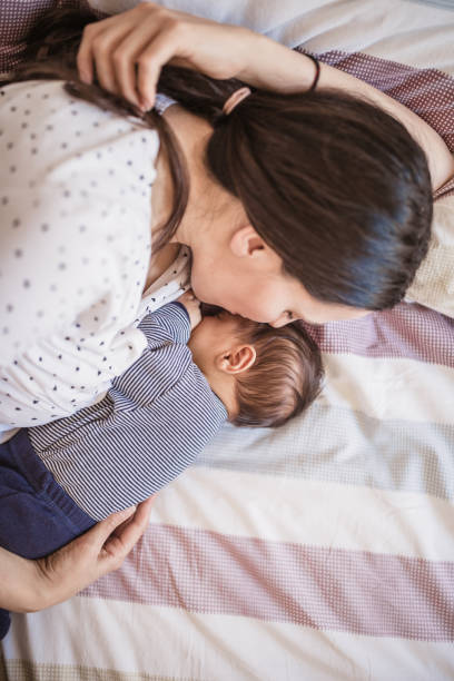 A tender moment captured from above, showing a mother lovingly laying beside her infant baby on a cozy bed, epitomizing the intimate bond between a mother and child.