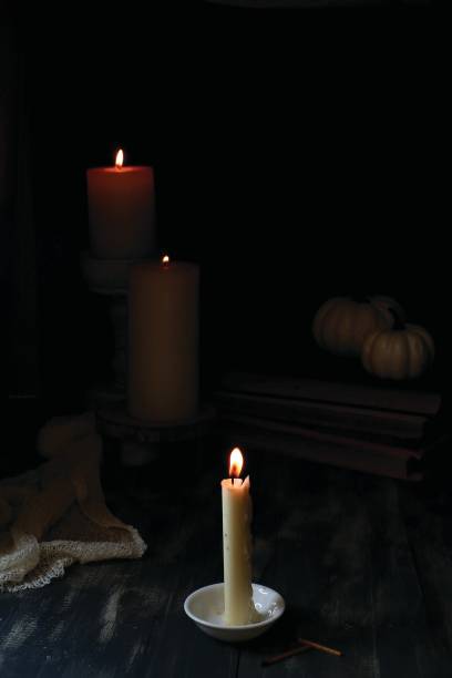 istock A lit candle on a white saucer with two larger lit candles behind it - dark background 2187634730