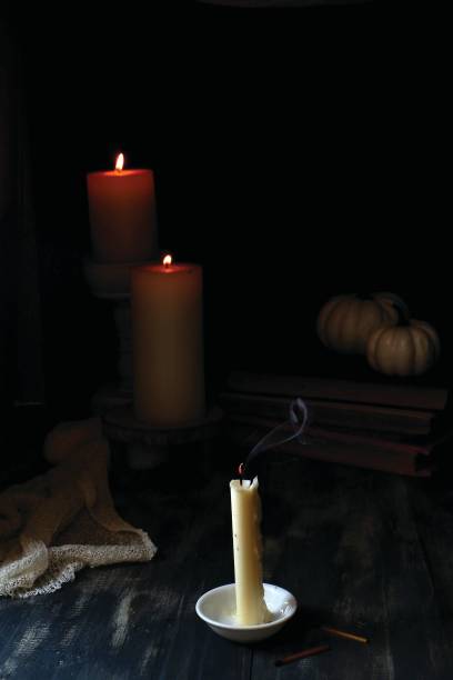 istock A recently extinguished candle on a white saucer with visible smoke effects, and two larger lit candles in the background - dark background. 2187634731