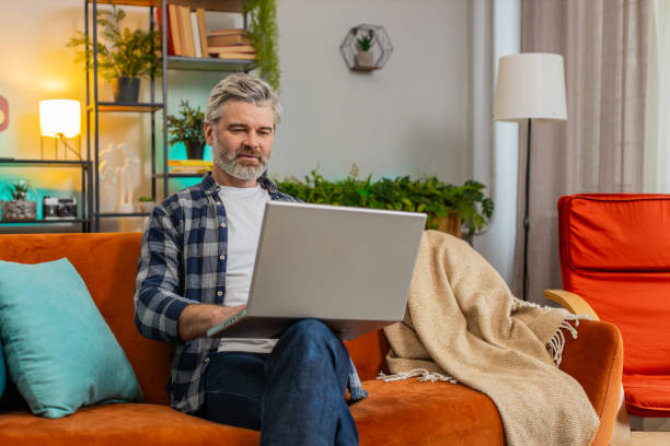 istock Strict middle-aged mature man typing on laptop browsing internet using apps sitting at home sofa 2187642882