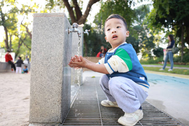 Hot summer day in the city. Little boy is having fun playing in the park fountain. He is running barefeet getting wet and splashing.