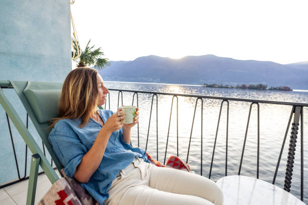 istock Woman Relaxing on Balcony with Coffee at Lakeside Sunset 2187650213