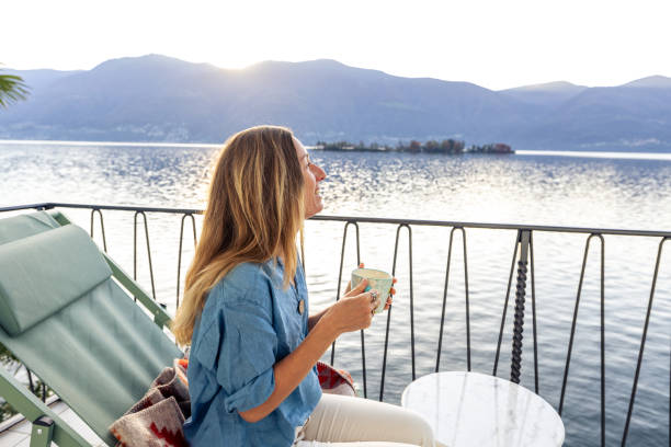 istock Woman Relaxing on Balcony with Coffee at Lakeside Sunset 2187650214