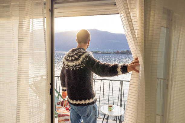 istock Welcoming the Day: Man in Sweater Opens Curtains to Stunning Lake View 2187650317