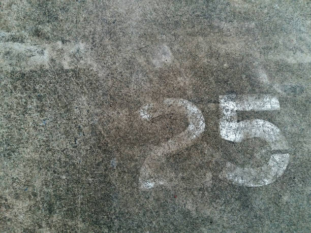 istock Number 25 or Twenty five number in white painted on the gray concrete wall or surface of street with copy space. Background concept 2187652273