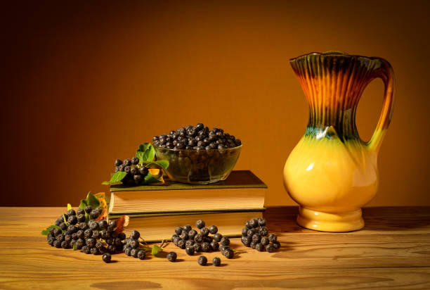 Still life, chokeberry, book and ceramic jug in studio on wooden table