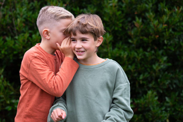 istock Children telling each other a secret and smiling outdoors with copy space 2187670077