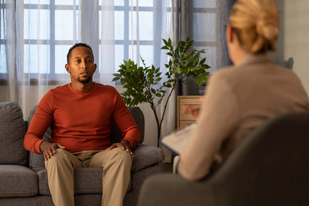istock Focused man engages deeply in conversation with counselor, seated on grey couch, thoughtful. 2187671223