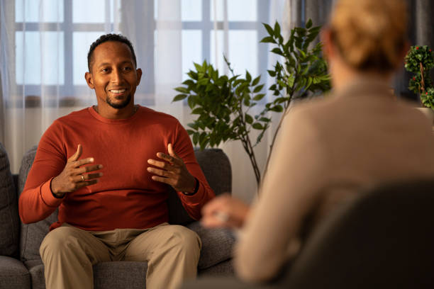 istock Man engaging in animated conversation seated on a grey couch with hand gestures experienced. 2187671257