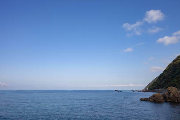 A calm coastal landscape with the soft morning light illuminating the sea surface and calm waves lapping at the sandy beach. The clear air and gentle sound of waves spread out, giving the impression of a quiet celebration of the beginning of the day.