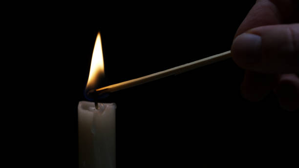 istock Hand lighting candle with match on black background 2187676935