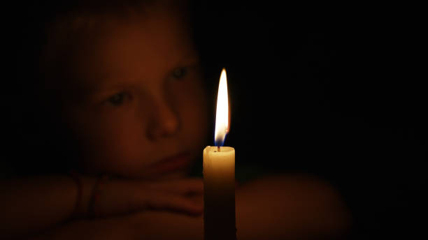 istock Child Gazes Intently at a Flickering Candle Flame in Dim Light 2187676956
