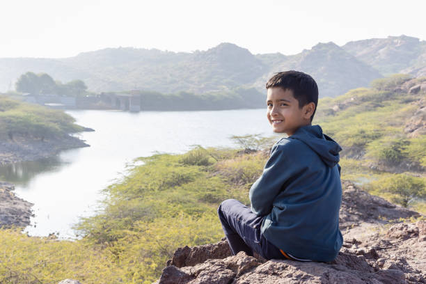 Smiling Young Boy Sitting at Mountain Top with Lake View