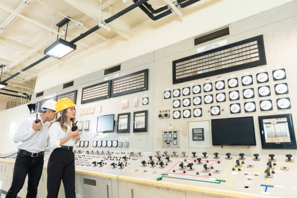 istock Two Asian male and female engineers walk around and analyze structures in a large industrial wind and water power plant, wearing hard hats and with electrical panels in the machine room. 2187694336
