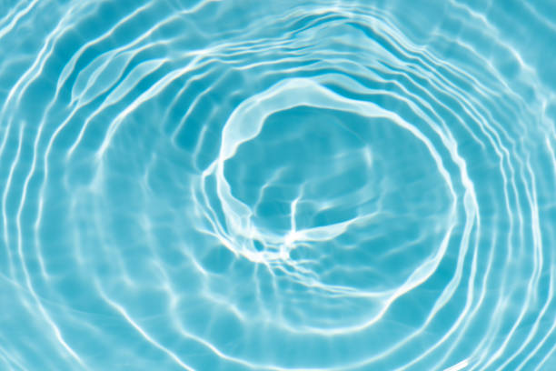 Blue water with ripples on the surface. Defocus blurred transparent blue colored clear calm water surface texture with splashes and bubbles. Water waves with shining pattern texture background.