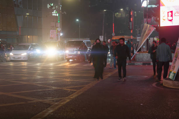 Captured on December 31, 2022, in Gulshan, Dhaka, this image showcases a busy city intersection at night. The red traffic signal has caused vehicles to halt, while pedestrians are seen crossing the road. The scene is illuminated by the headlights of waiting cars and street lights, highlighting the bustling urban nightlife and the dynamic interaction between traffic and pedestrians in a major city.