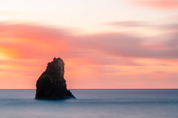 The sky and the rocky shore light up in the warm colors of sunset on the coastline just north of Cape Town, South Africa. Motion of the sea is blurred by a long exposure.