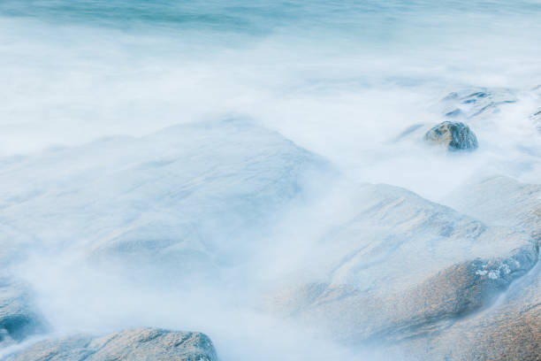 Soft and misty effect created by long exposure of ocean waves against rocks at sunset.